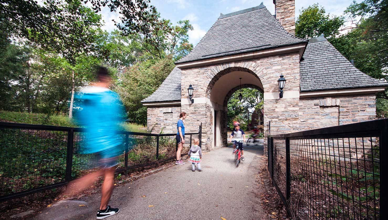 Frick Park's stone gatehouse with people walking and biking through