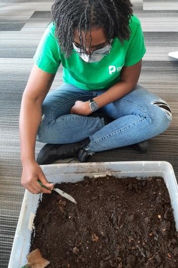 An image of a person demonstrating dirt exploration with a bin of dirt and shovel