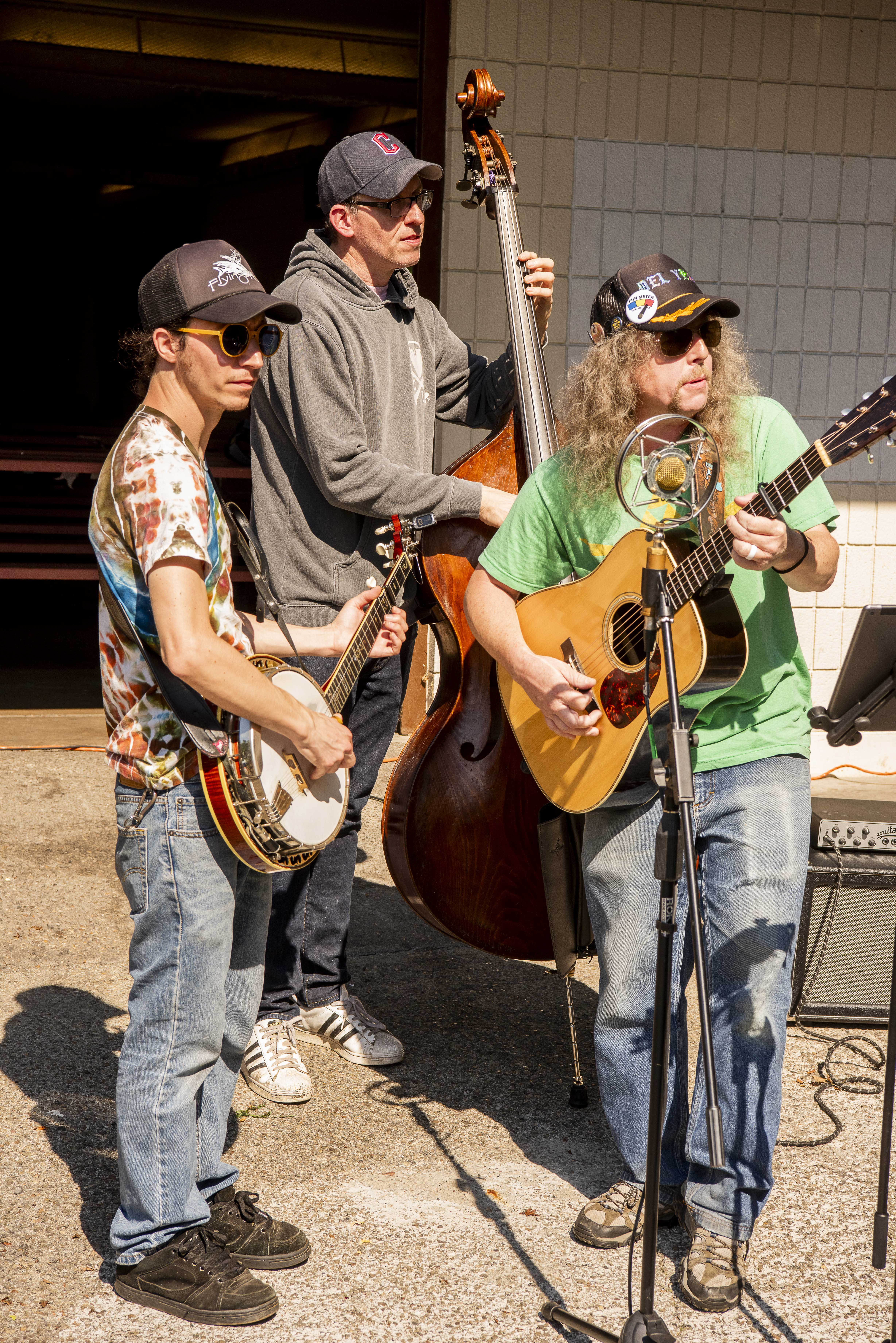 A musical trio, holding a guitar, a banjo, and a double bass, play music.