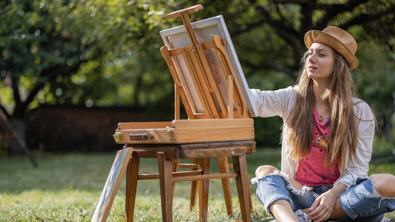 A person sits down and paints at an easel outside.