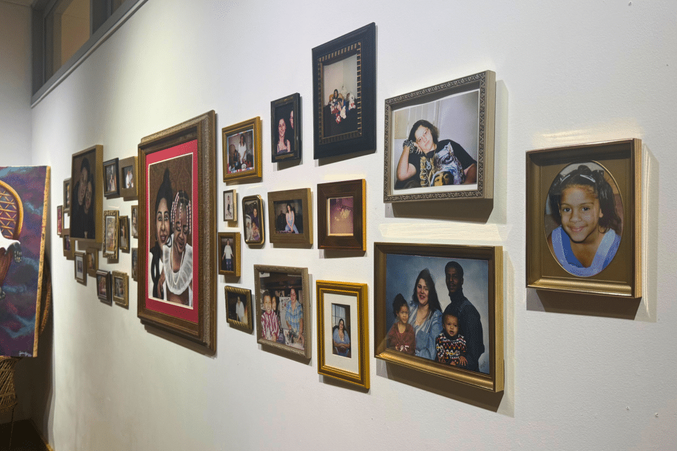 A gallery wall depicts framed family photos of various sizes, in gold frames. They seem to all belong to one family.