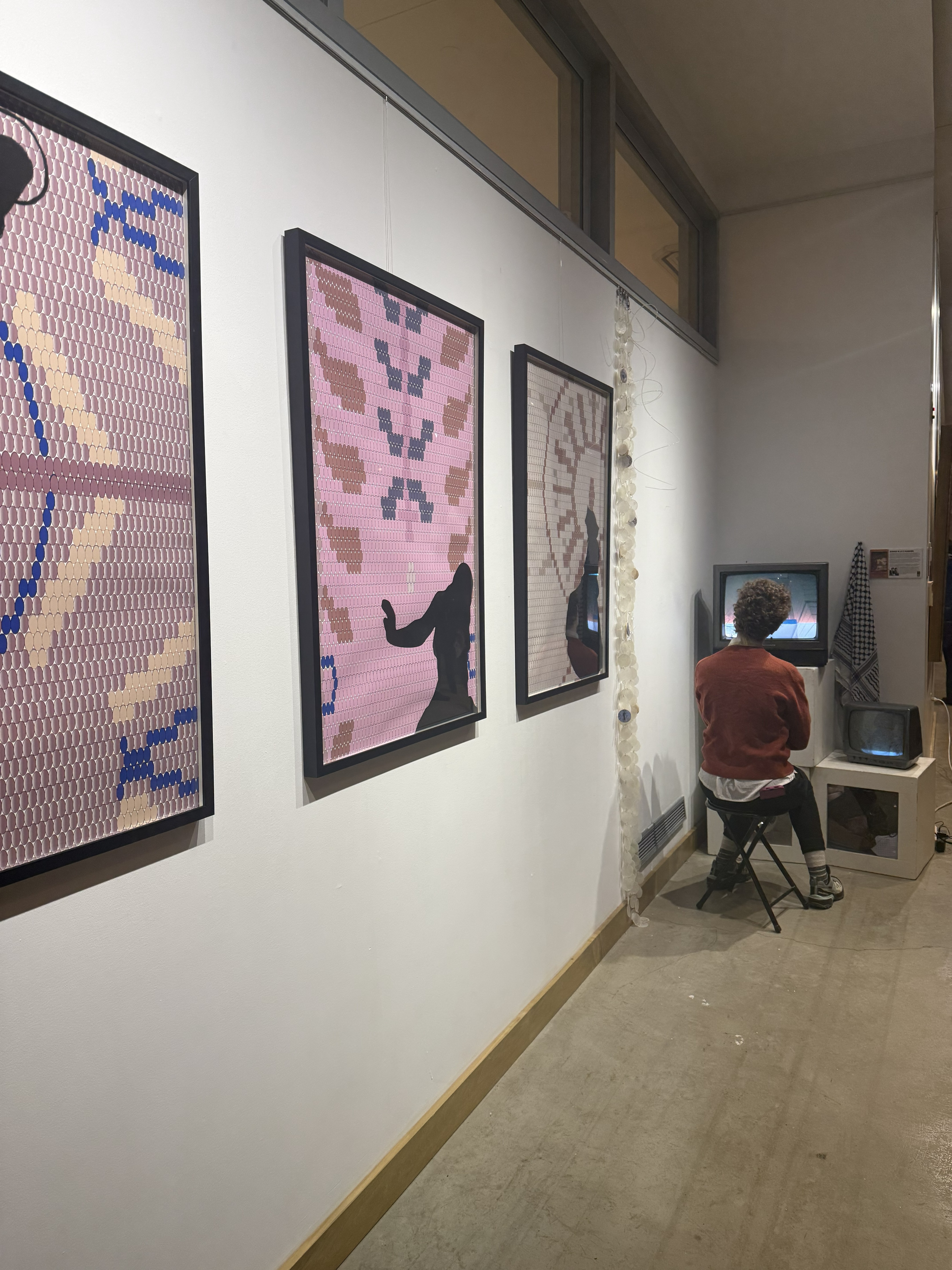 A seated person watches a video installation and along the wall are purple, textured digital collages.